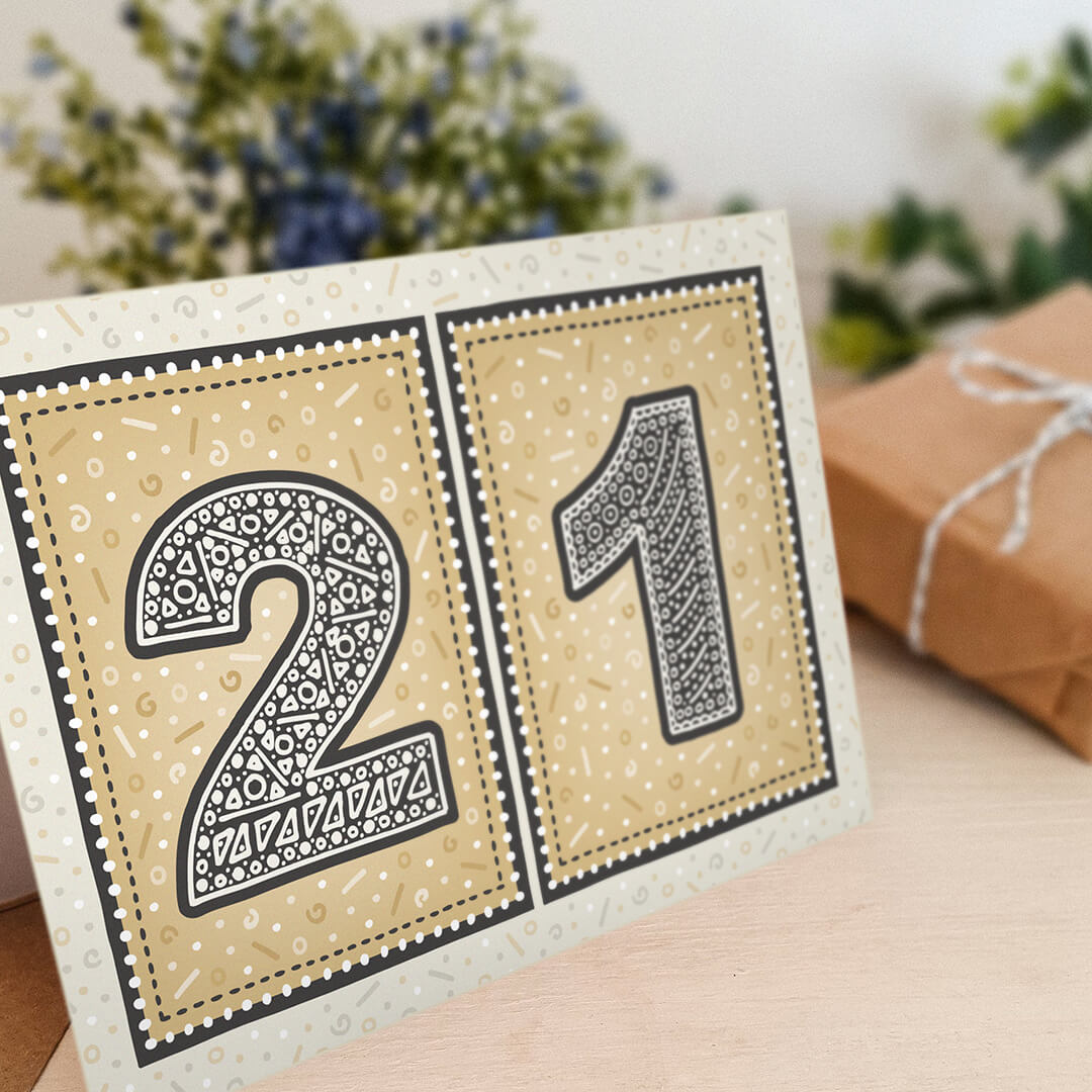 unique black and gold 21st birthday card with flowers and gifts wrapped in kraft brown paper in the background