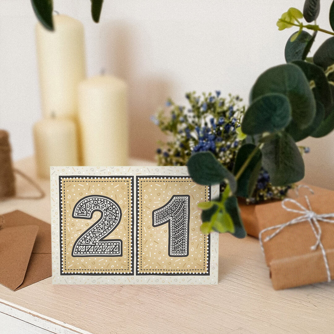 unique black and gold 21st birthday card sat on white dresser with candles, plants and gifts