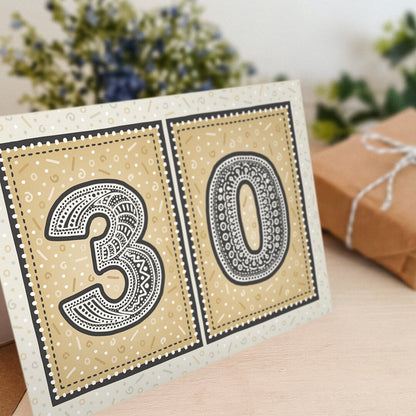 unique black and gold 30th birthday card with flowers and gifts in background
