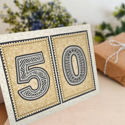 unique black and gold 50th birthday card with flowers and gifts in the background