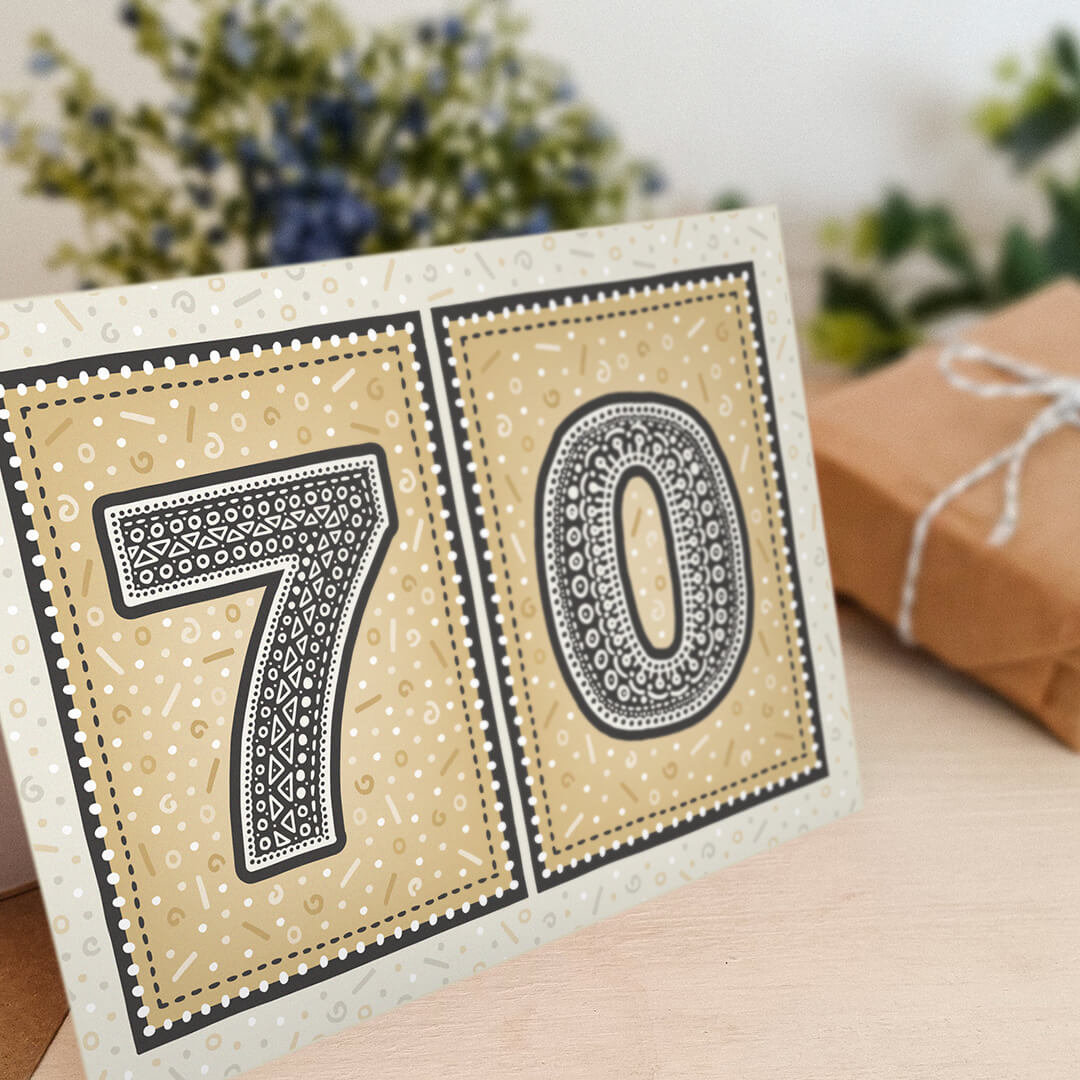 unique black and gold 70th birthday card with flowers and gifts in the background