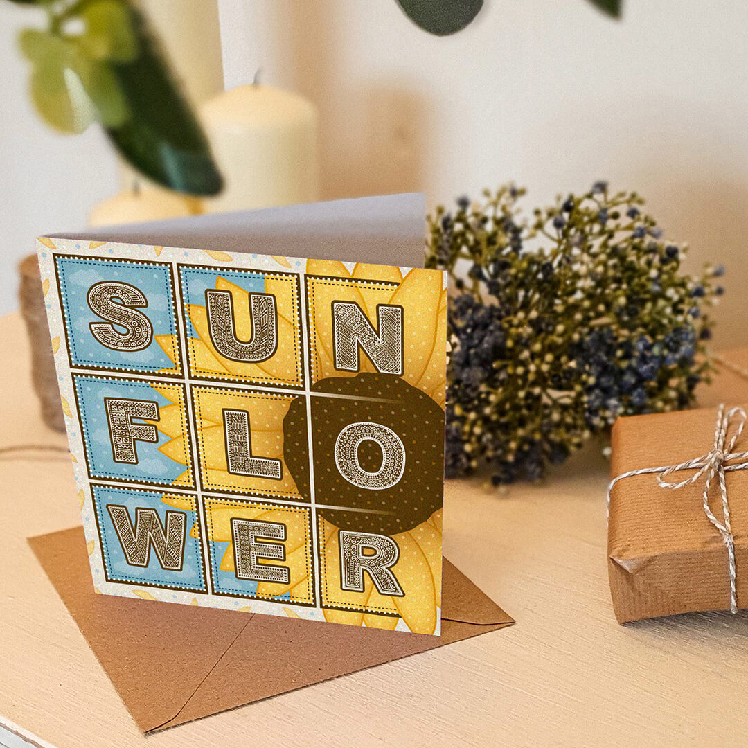 Blue and yellow sunflower greeting card with sunflower illustration on a white wooden dresser with a gift and blue flowers in the background