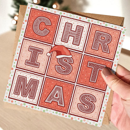Red Christmas card with 'Christmas' text and a Santa hat illustration held by a hand.