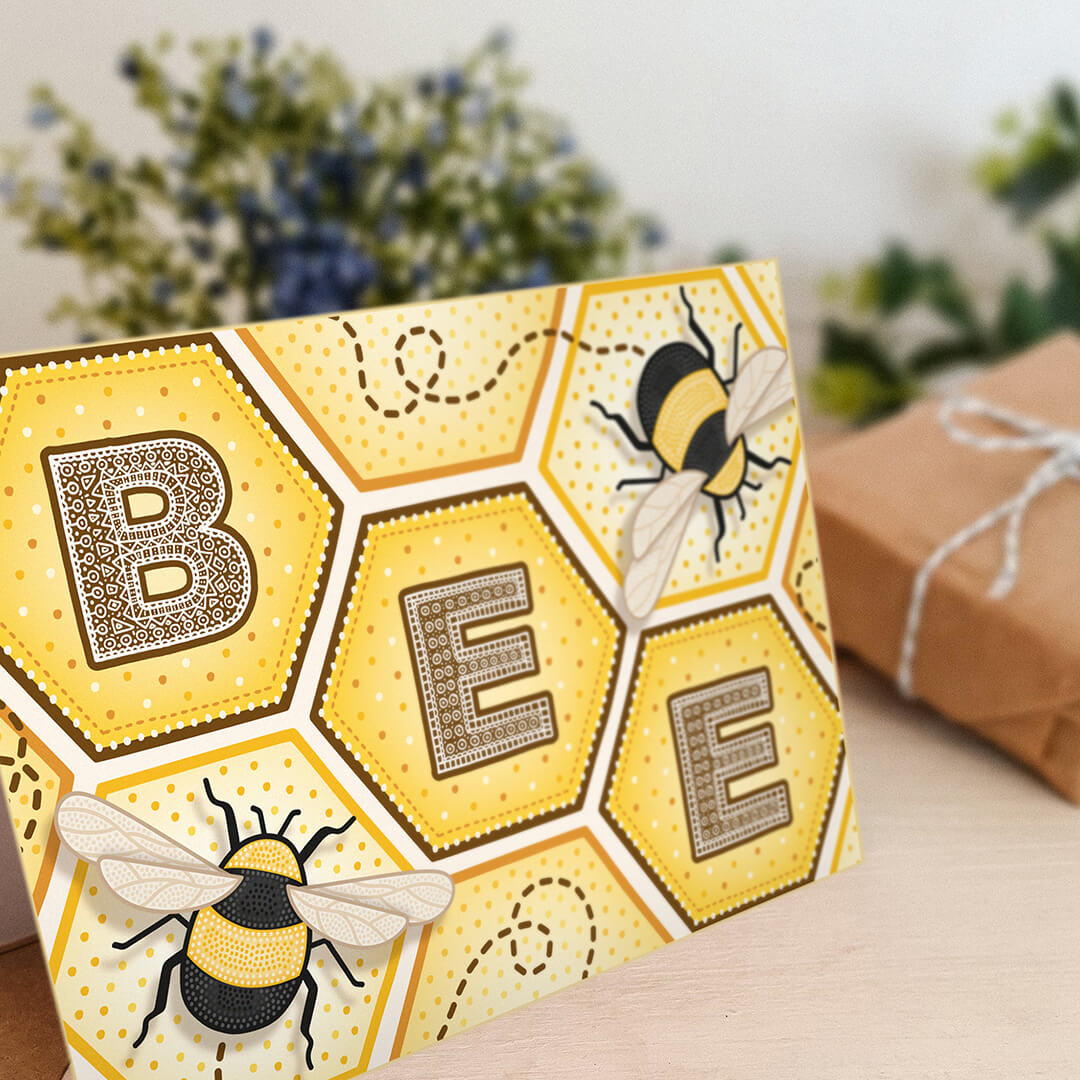 Bee greeting card with bee illustrations and honeycomb design on a white wooden dresser with a blurred background