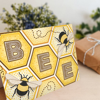 Bee greeting card with bee illustrations and honeycomb design on a white wooden dresser with a blurred background