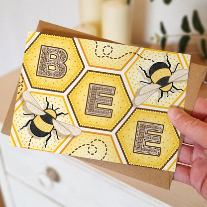 Bee greeting card with bee illustrations, detailed typography and honeycomb design held by a hand