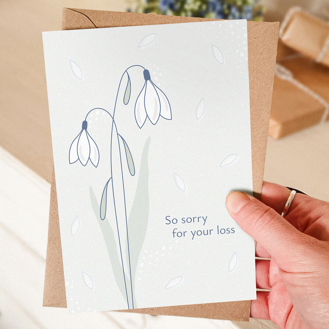 hand holding white snowdrops sympathy card with blurred background