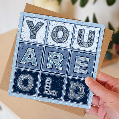 hand holding funny you are old man birthday card Blue typographic birthday card for old man Supplied with kraft brown recycled envelope Blank inside