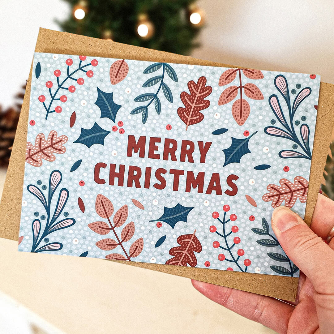 Hand holding unique botanical Christmas card with festive foliage illustrations of holly, berries and mistletoe Printed on recycled card Supplied with kraft brown recycled envelope