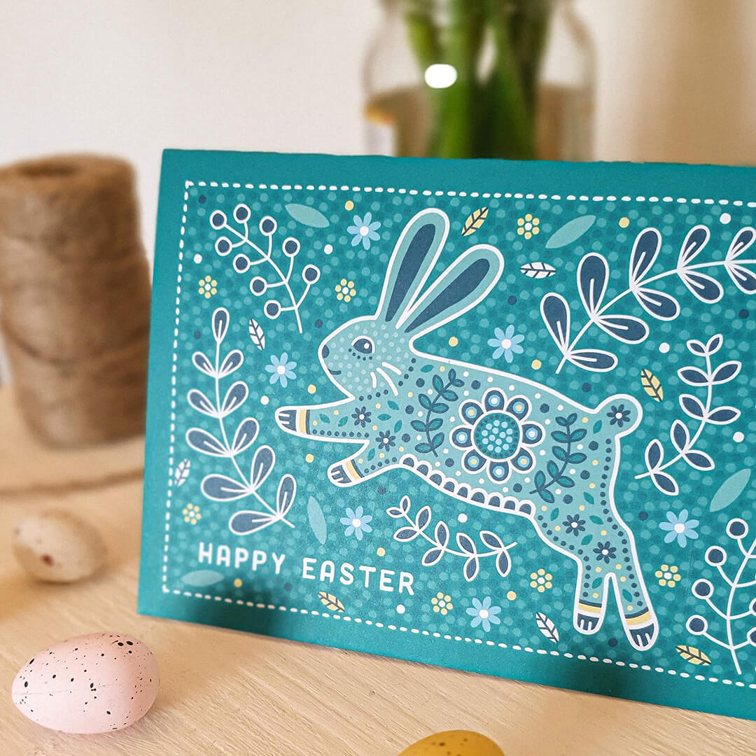 Turquoise illustrated Easter Bunny card Printed on recycled card Featuring folk art illustrations of plants and nature with Easter Bunny jumping through grass