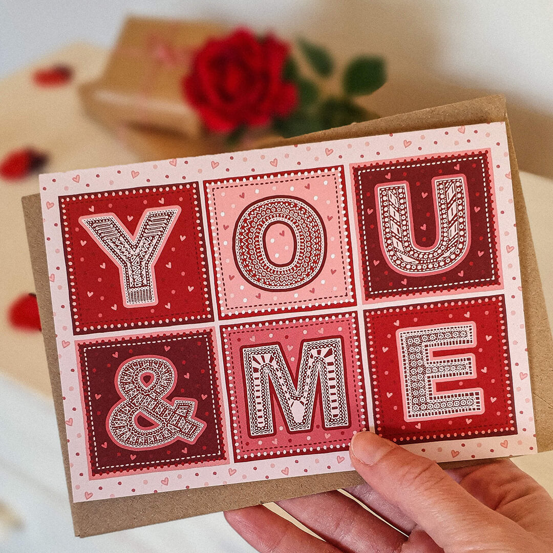 Hand holding red and pink typographic valentine's day card for boyfriend Unique typographic You & Me design Printed on recycled card Supplied with kraft brown recycled envelope